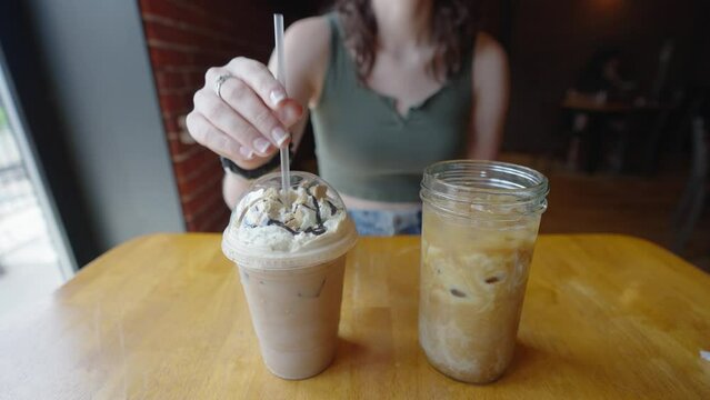 Comparing a plastic cup and straw to a glass cup with coffee. Coffee in a glass mason jar and a frappuccino in a plastic cup with a lid and straw.