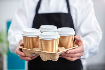 Waiter barista holding a take out paper disposable cup of hot coffee in cafe