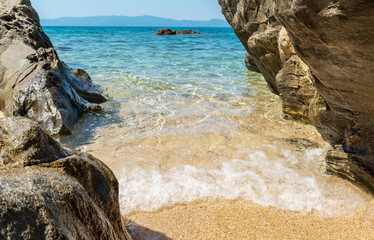 Deserted beach near Ouranoupoli, Athos peninsula, Chalkidiki, Greece. Crystal clear water in blue sandy lagoon between rocks. Idyllic summer seascape of Aegean Sea on Halkidiki, travel and vacation