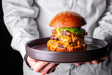 chef holding big triple cheeseburger on a tray in hand