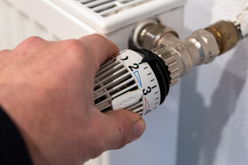 Male hand turns a radiator thermostat