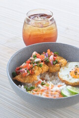 chicken katsu sambal matah with sunny side up egg and a glass of ice tea on a wooden table.
