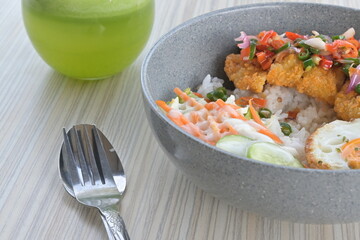 chicken katsu sambal matah with salad and a glass of pineapple mustard juice on a wooden table.