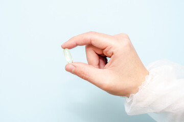 Doctor's hand holding a fish oil capsule (Omega 3) or pill isolated on light blue background