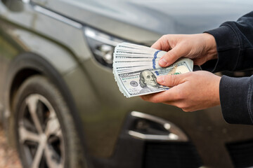 Person with money in the hand stands front car. Insurance, loan and buying car concept