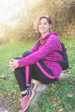 Portrait of smiling woman with backpack sitting on rock in forest