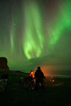 Sitting Around An Campfire With Northern Lights - Aurora Borealis In The Sky Overhead, Unstad, VestvÃ¥gÃ¸y, Lofoten Islands, Norway