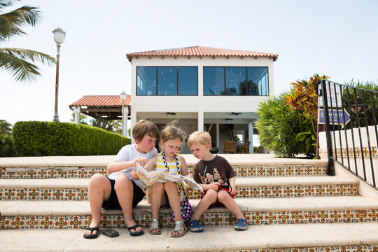 Three Siblings Look at a Map, Sitting on Tropical Steps in Caribbean