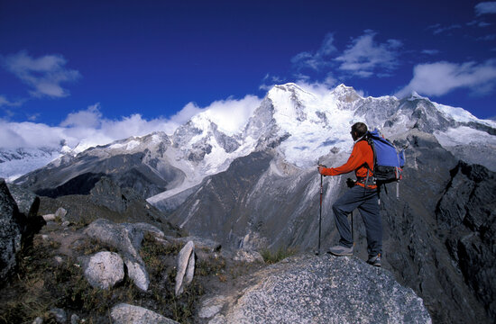 Man standing on a peak looking out at snow covered mountains in Cordillera Blanca, Peru.