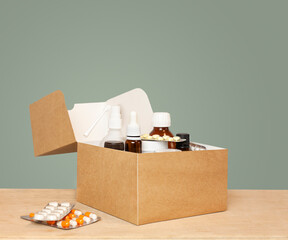 paper box with medicines on a wooden table against a green wall
