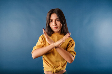 Portrait of young brunette woman wearing mustard yellow t-shirt isolated over blue background...