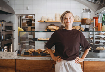 Portrait of smiling young woman entrepreneur standing at the counter of her bakery and coffee shop. Local small business owner indoors.