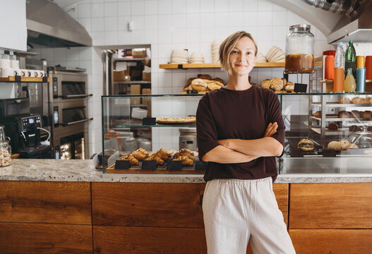 Portrait of smiling young woman entrepreneur standing at the counter of her bakery and coffee shop. Local small business owner indoors.