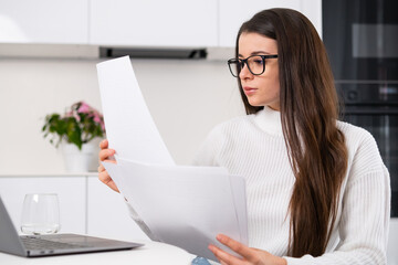 Cheerful lady holding paper uses a computer and works remotely. Distance freelance job concept.