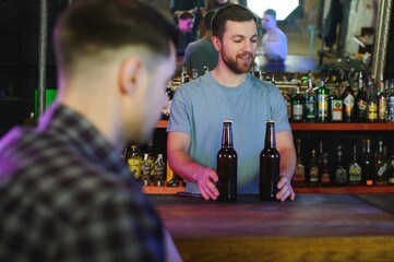 Barman bottle of beer. Nearby empty glass on wooden bar counter in interior of pub, cropped, free space.
