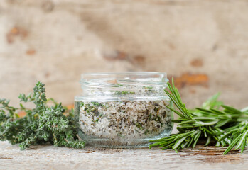 Homemade sea salt scrub with olive oil, rosemary and thyme (bath salt, foot soak, facial or hair mask) in a glass jar. Natural beauty treatment and spa recipe. Copy space, old wooden background.