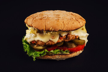 Cheeseburger with cheese sauce and pickled cucumbers on a black