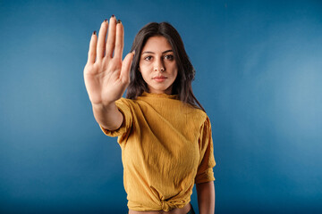 Portrait of cute dark-haired woman wearing casual top isolated over blue background doing stop sing...