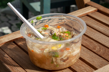Chicken and mushroom soup in a cheap clear plastic container with a spoon. Affordable lunch in disposable bowl to go