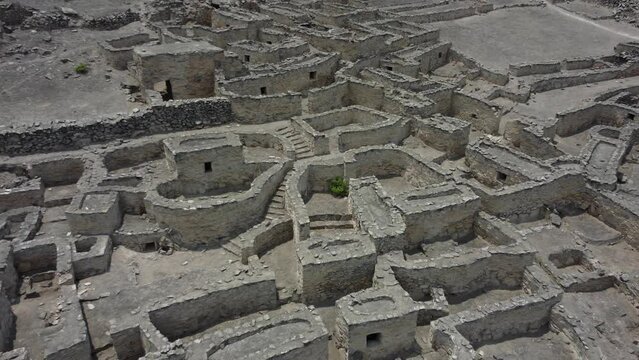 Drone video of a 500 year old abandoned stone town on a mountain side. Drone flies back from a green plant in the middle of maze of houses, paths and stairs. Located in Lurin district of Lima, Peru.