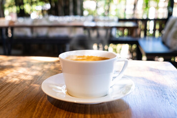 White cup of hot coffee with smoke above place on desk with bokeh in the background