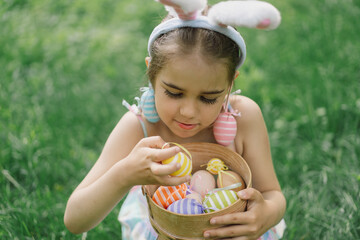 Easter egg hunt in spring garden. Funny girl with eggs basket and bunny ears on Easter egg hunt in garden. Children celebrating Easter. Happy easter card