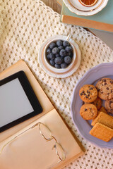 Plate of cookies, cup of tea, fresh blueberries, dry oranges, stack of books, reading glasses and tablet on the table. Hygge at home. Flat lay.