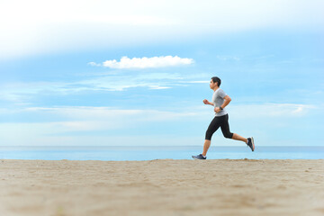 Asian man jogging  on tropical sandy beach with blue sea and clear sky background.
