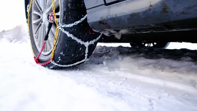 Snow chains on tire at winter road. Snow chains on the tire of a white car in winter on the snow. Winter bringing dangerous driving conditions for vehicles without snow chains.