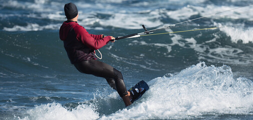 Naklejka premium Athletic man jumping on kite surf board on a sea waves. Kiteboarding man among waves quickly goes.Watersport adrenaline fun adventure acitivity