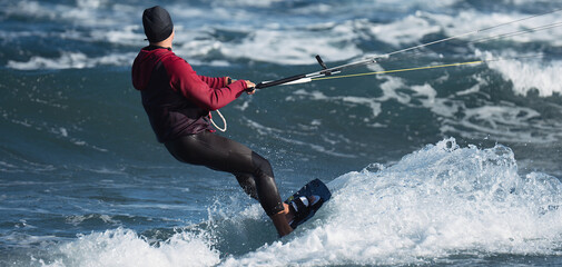 Athletic man jumping on kite surf board on a sea waves. Kiteboarding  man among waves quickly...