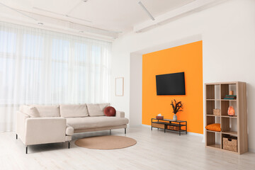 Stylish sofa and wooden furniture near orange wall in spacious room. Interior design