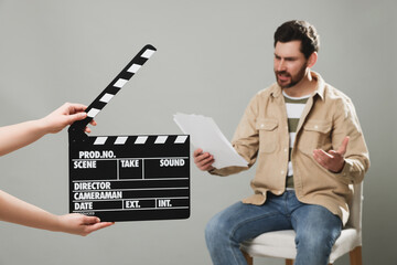 Emotional actor performing while second assistant camera holding clapperboard on grey background, closeup - obrazy, fototapety, plakaty