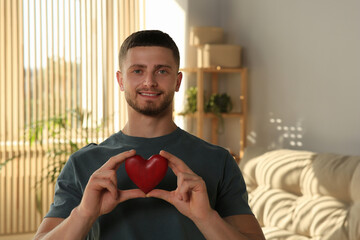 Happy volunteer holding red heart with hands indoors