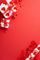Valentine's Day concept. Top view vertical photo of present boxes wrapping paper roll ribbon heart shaped candies and sprinkles on isolated red background with empty space