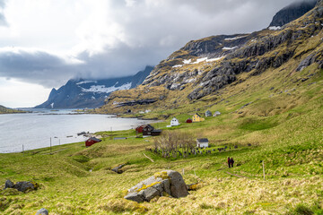 Vindstad village in Lofoten, Norway, small colored houses, big mountains and a bluish lake, during spring on a clear day with clouds	
