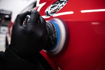 employee of a car detailing studio polishes the paintwork of a red car with an electric polishing machine