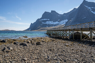 Wooden footbridge in the small port of Vindstad village in Lofoten, Norway, during spring on a clear day with clouds