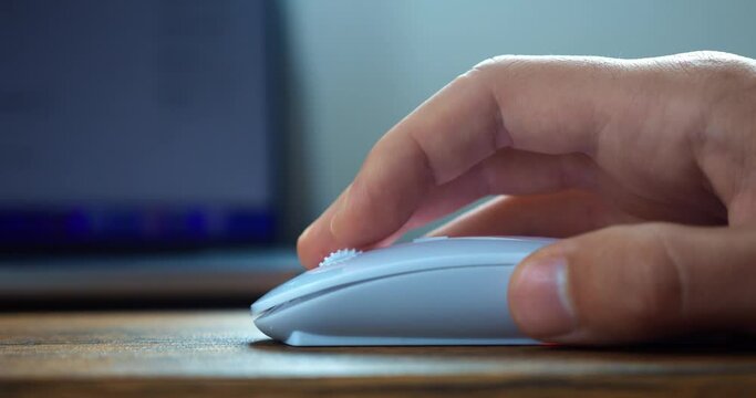Close up male hand uses white computer mouse, click and scroll the mouse roller, searching for information on the Internet, surfing web pages. Working at computer using handheld pointing device
