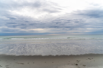 Waves coming onto the beach at Rambergstranda beach in Lofoten, Norway, during spring on a clear day with clouds