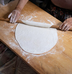 Rolling dough using rolling pin. Women's hands in flour roll out the dough with a rolling pin on the table.