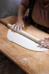 Rolling dough using rolling pin. Women's hands in flour roll out the dough with a rolling pin on the table.