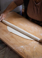 Rolling dough using rolling pin. Women's hands in flour roll out the dough with a rolling pin on the table.