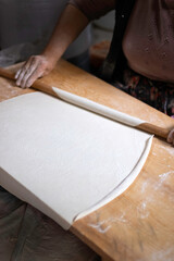 Rolling dough using rolling pin. Women's hands in flour roll out the dough with a rolling pin on the table.