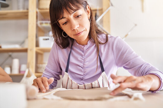 Woman potter with apron preparing clay slabs in a pottery workshop.. Craft, art and hobbies concept.