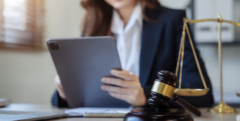 Justice and law concept. Female in office the gavel, working with digital tablet computer on wood table in sun light.