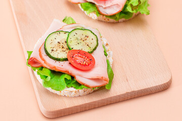 Light Breakfast. Quick and Healthy Sandwiches. Rice Cakes with Ham, Tomato, Fresh Cucumber and Green Salad on Wooden Cutting Board. Beige Background