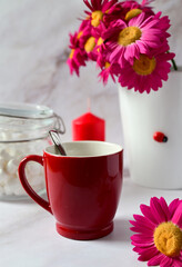 Fototapeta na wymiar red mug with tea on the background of a bouquet of red flowers