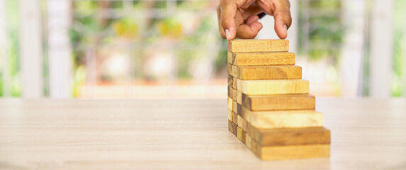 Hand placing wooden block tower stack in pyramid stair step with caution to prevent collapse or...