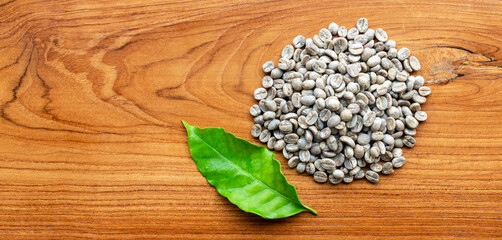 Top view of unroasted raw coffee beans or Dried green coffee beans and green coffee leaf  on wooden background